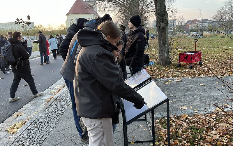 Schülerinnen und Schüler schau auf Informationstafeln, auf der Straße und auf dem Gehweg stehen weitere Teilnehmende an der Veranstaltung.