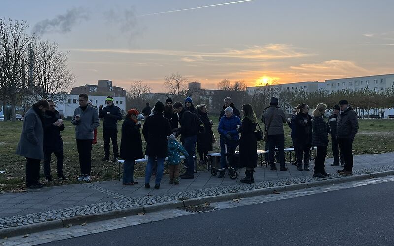 Nach der Veranstaltung reden die Teilnehmenden miteinander, inzwischen tritt die Dämmerung ein. Am klaren Himmel ist die Fluglinie eines Flugzeugs zu sehen.