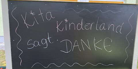 Auf einer schwarzen Tafel steht mit weißer Kreide "Kita Kinderland sagt DANKE" geschrieben. 