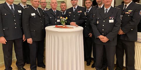 11 uniformierte Feuerwehrmänner stehen hinter einem weißen Tisch.