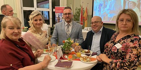 Die Forster Rosenkönigen steht mit anderen Besuchern an einem Tisch,