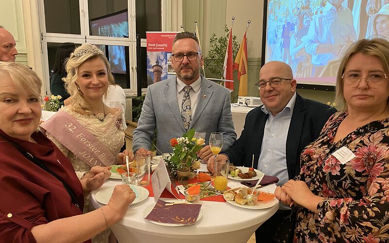 Die Forster Rosenkönigen steht mit anderen Besuchern an einem Tisch,