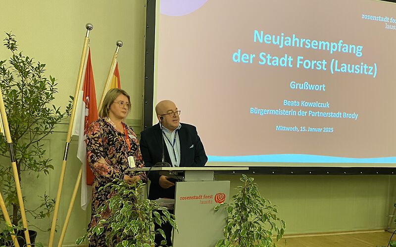 Die Bürgermeisterin der Partnerstadt Brody hält an einem Podium eine Rede, auf einer Leinwand ist ihr Beitrag angekündigt.