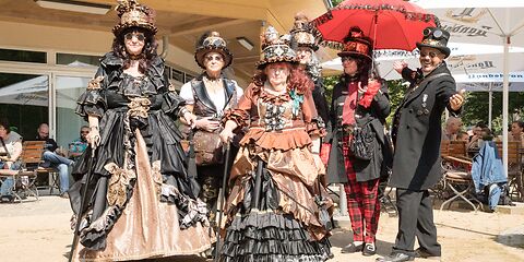 Vor dem Restaurant Rosenflair stehen 6 Personen in Steampunk-Outfits (Kleider bzw. Anzug).