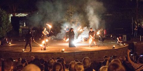 Die Feuershow auf der Wehrinselbühne, mehrere Männer mit Stangen, an deren Enden Flammen brennen. 