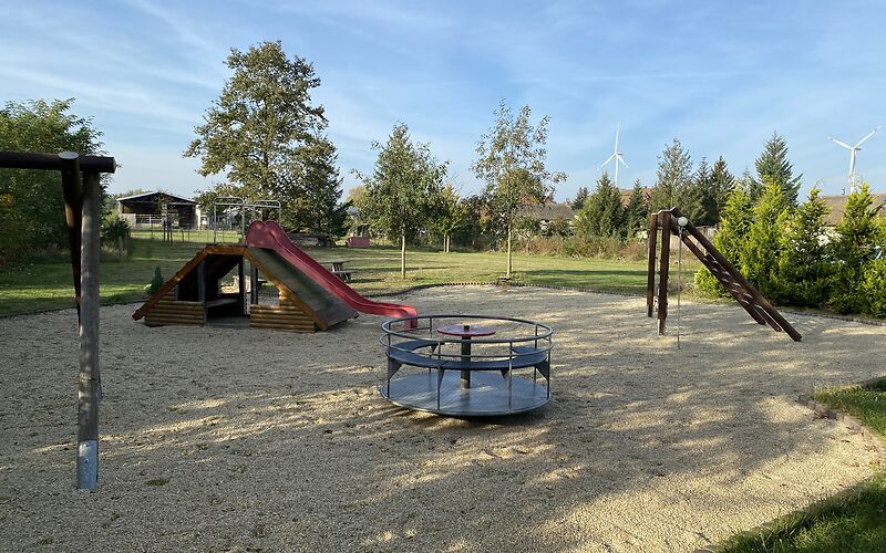 Mittig steht das Karussel, rechts ist das Klettergerüst und links die Rutsche, die an einer überdachten Holzbank befestigt ist.